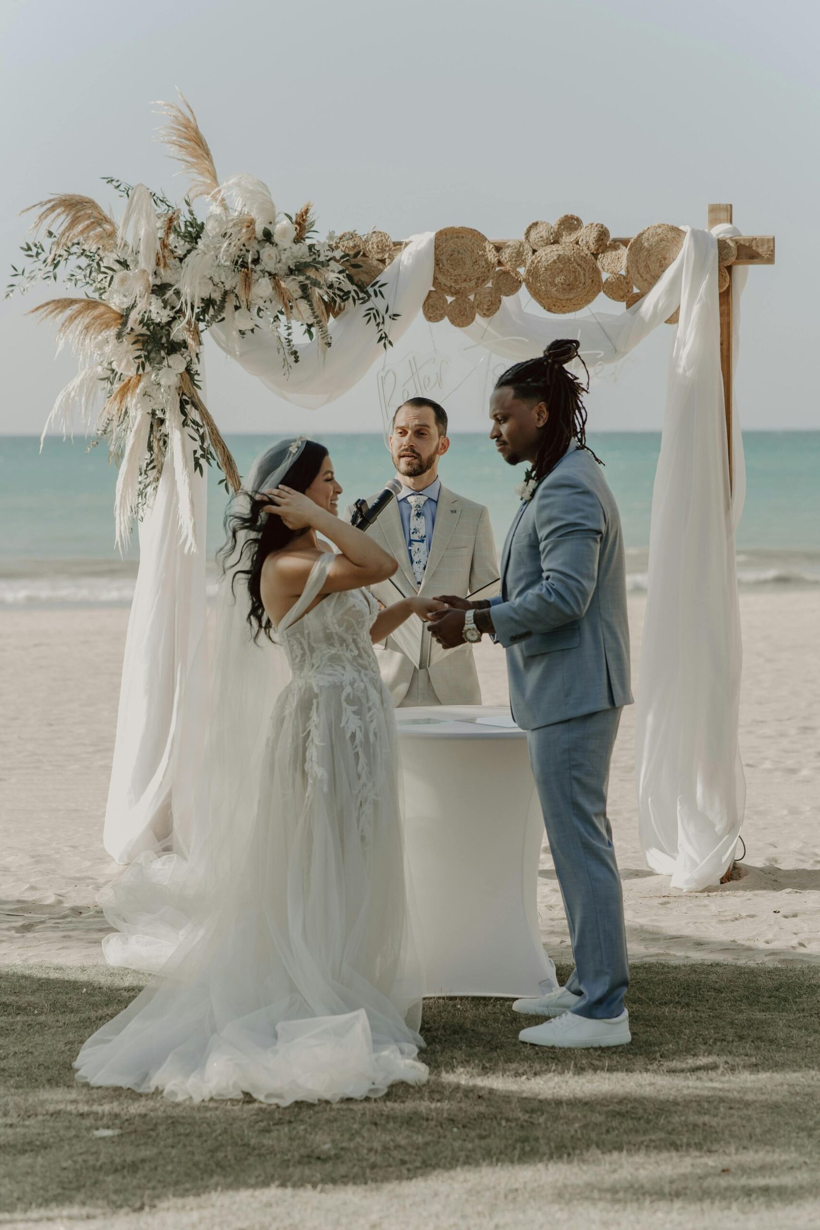 A stunning beachfront wedding ceremony featuring a bride, groom, and officiant under a floral arch.